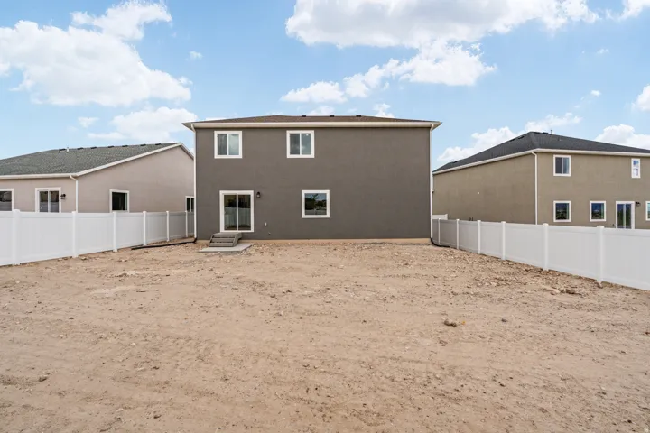 Expansive rear yard with privacy fencing and a two-story residence featuring a sliding glass door and windows