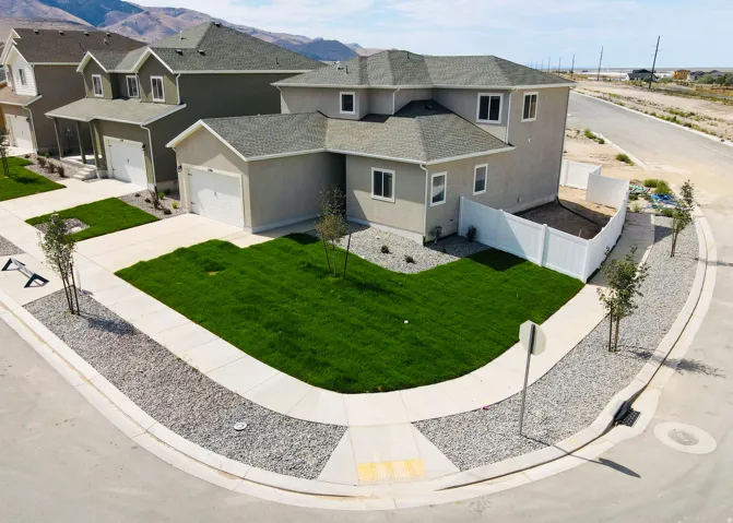 Contemporary stucco residence featuring a two-car garage, white vinyl fencing, a newly sodded lawn, and mature landscaping elements