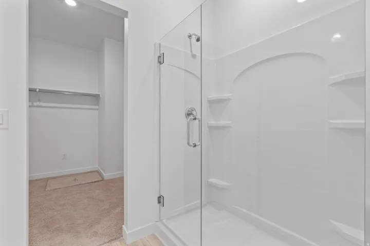 Shower enclosure featuring a clear glass door, chrome hardware, integrated shelving, and a white finish