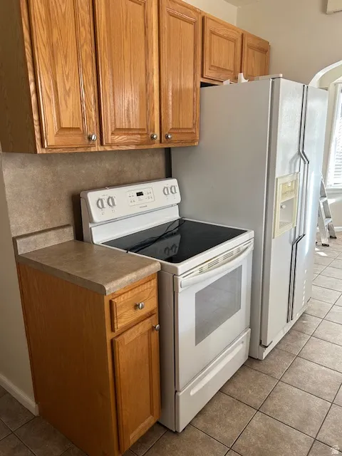 Kitchen featuring white appliances, light tile patterned floors, wood finish cabinets, and arched walkways