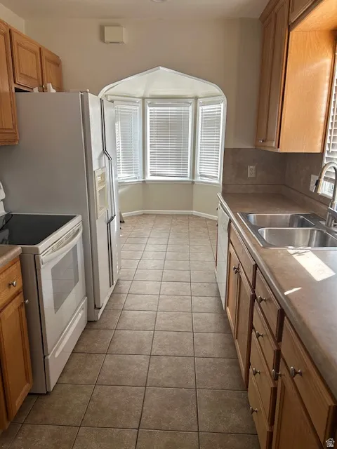 Kitchen with white electric range, dark tile patterned floors, wood finish cabinets, arched walkways, and dishwashing machine