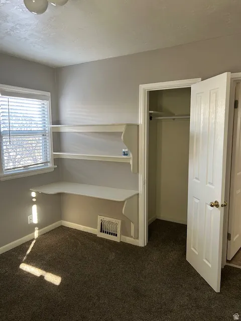 Unfurnished bedroom with dark colored carpet, a closet, and a textured ceiling
