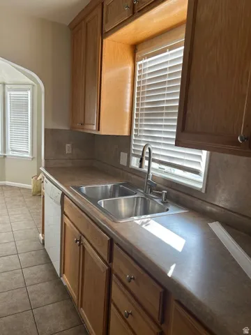 Kitchen featuring dark countertops, dark tile patterned flooring, white dishwasher, and backsplash