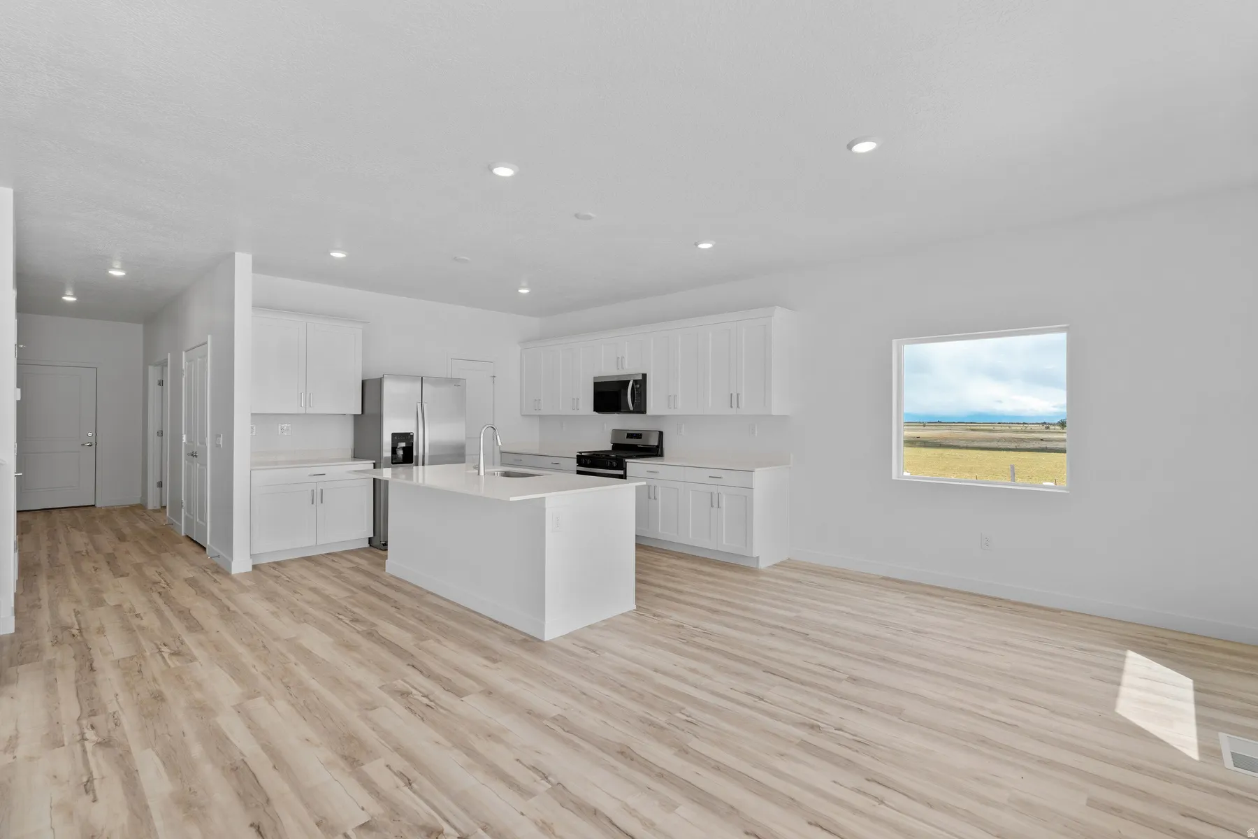 Open-concept kitchen featuring an island, white cabinetry, integrated stainless steel appliances, and wood-finish flooring