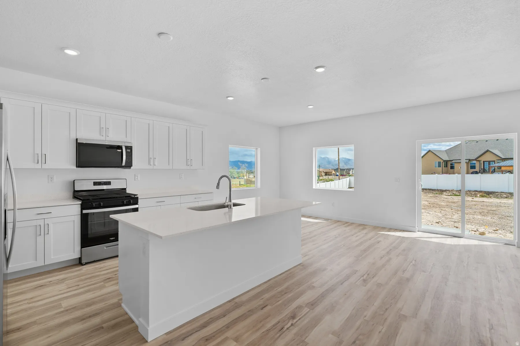 Open-concept kitchen and living area featuring a central island with an integrated sink, white cabinetry, and stainless steel appliances