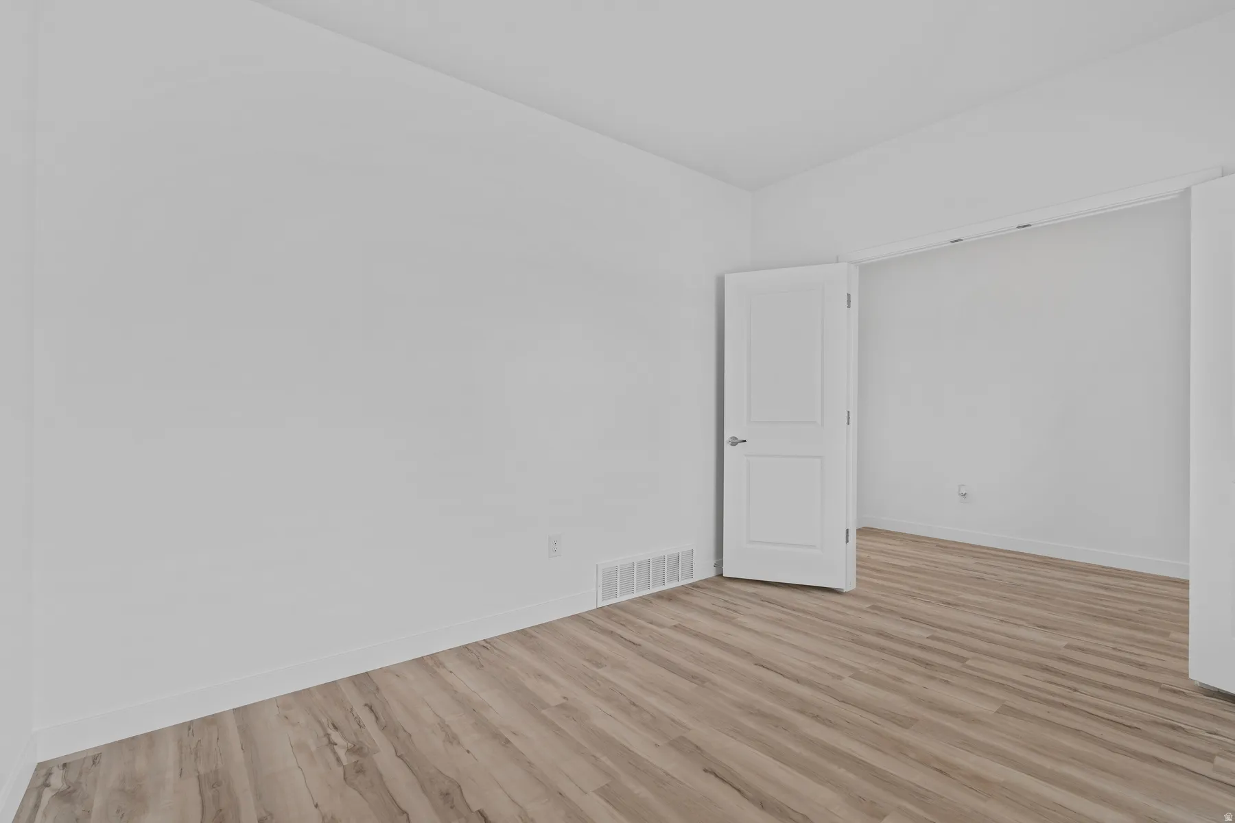 Bright interior featuring wood-finish flooring, white baseboards, and a white interior door with a silver handle