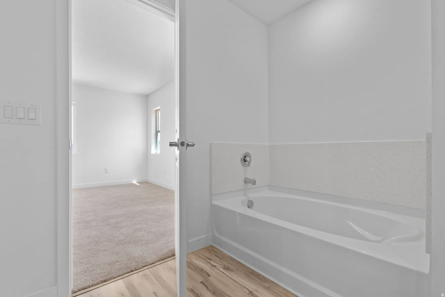 Freestanding bathtub with chrome fixtures, a tiled surround, and wood-finish flooring