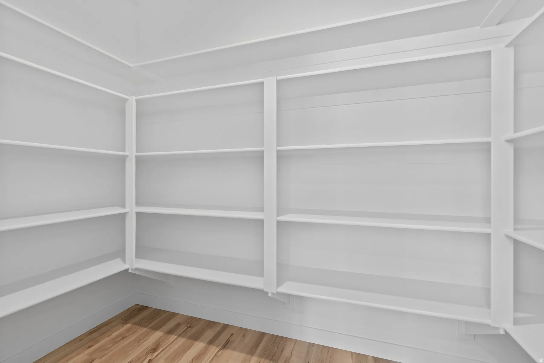 Built-in shelving unit featuring multiple white painted shelves, detailed trim work, white painted walls, and wood-finish flooring