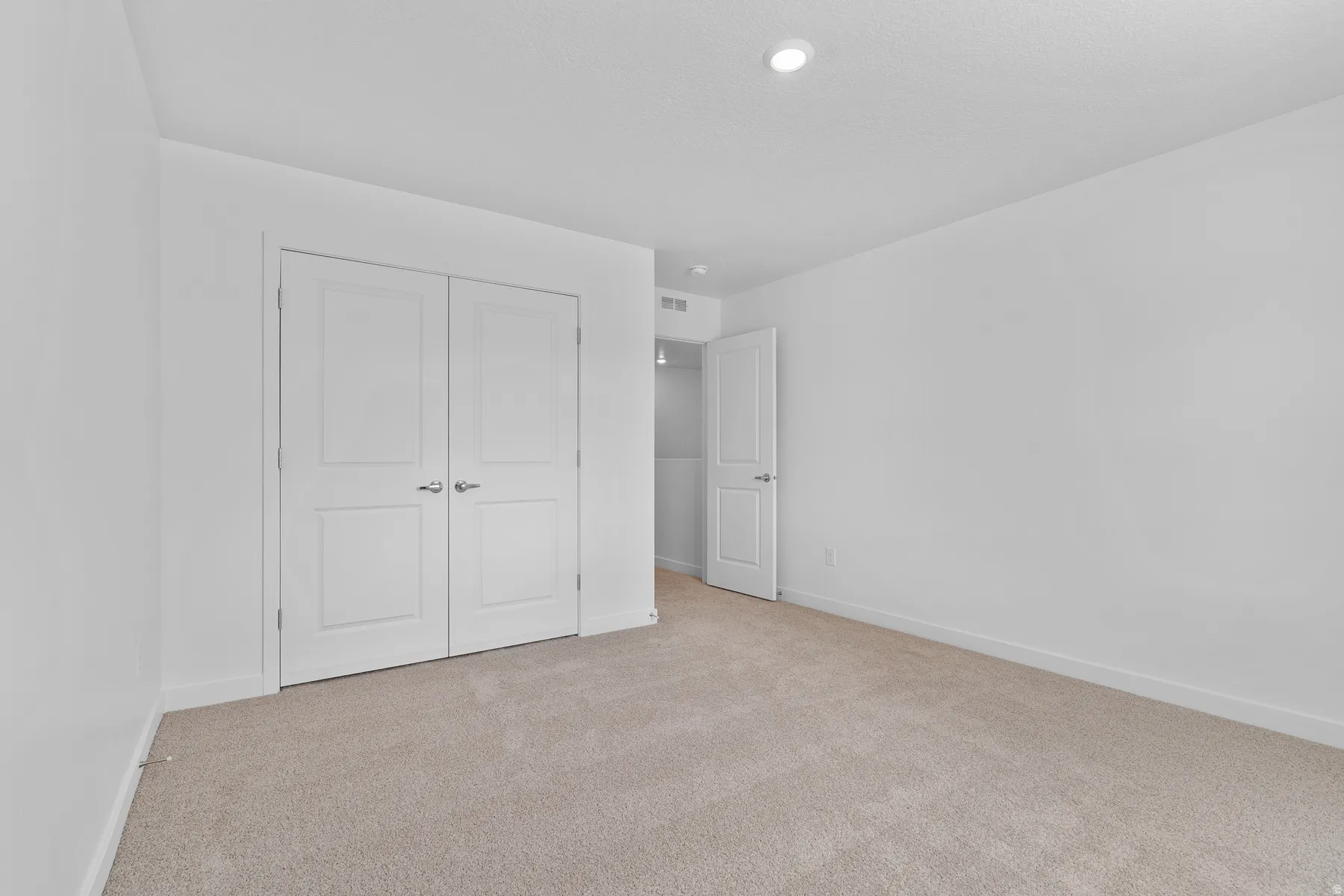 Bedroom featuring neutral carpeting, white walls, recessed ceiling lighting, and a double-door closet with paneling