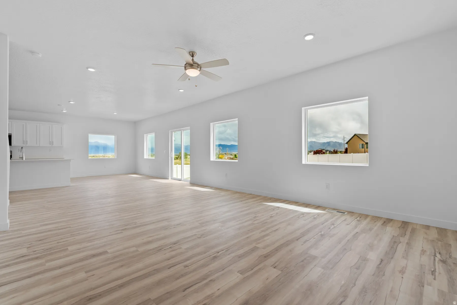 Spacious open-concept room featuring light wood-finish flooring, recessed lighting, and a ceiling fan
