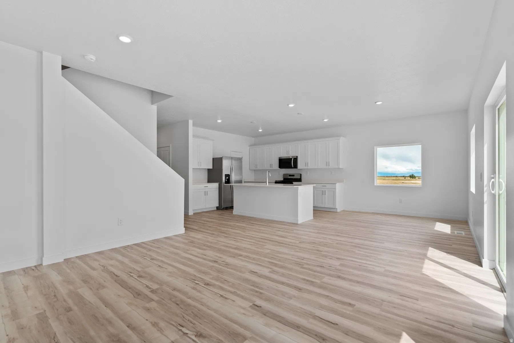 Open-concept interior featuring light wood-finish flooring, recessed lighting, and a contemporary kitchen with white cabinetry and stainless steel appliances