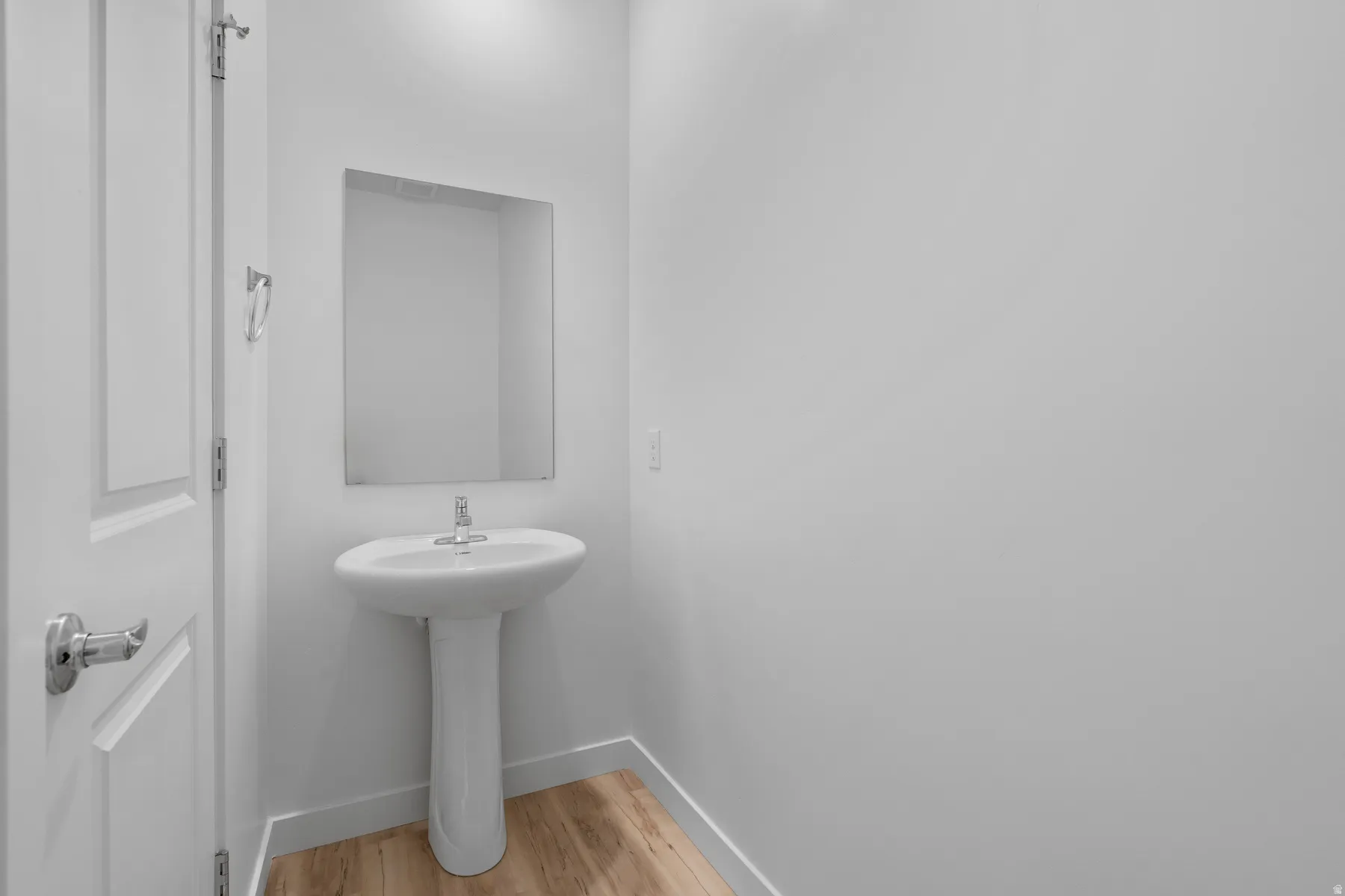 Pedestal sink with chrome faucet, framed mirror, and light wood-finish flooring