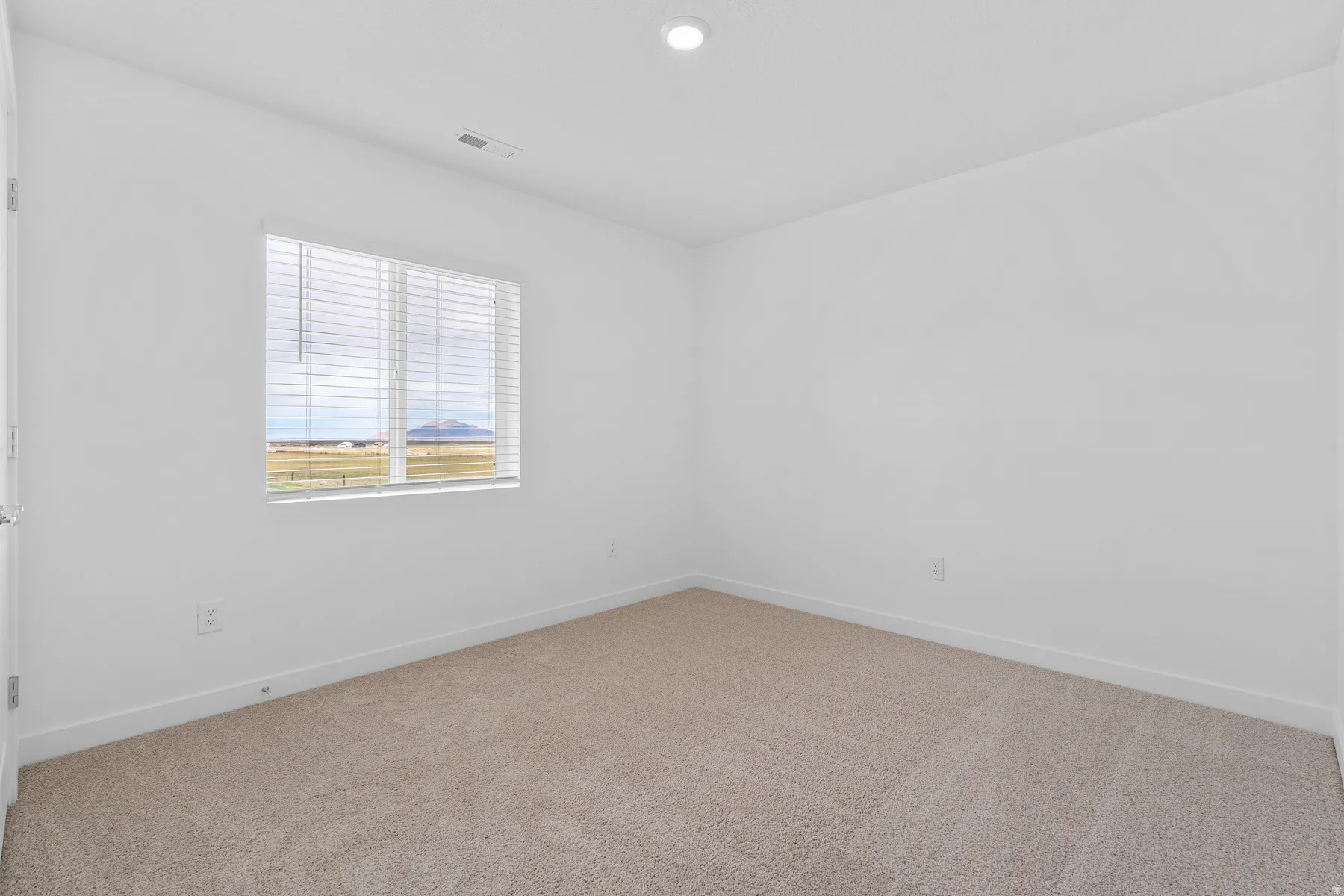 Carpeted room featuring a window with horizontal blinds, providing natural light and a distant landscape