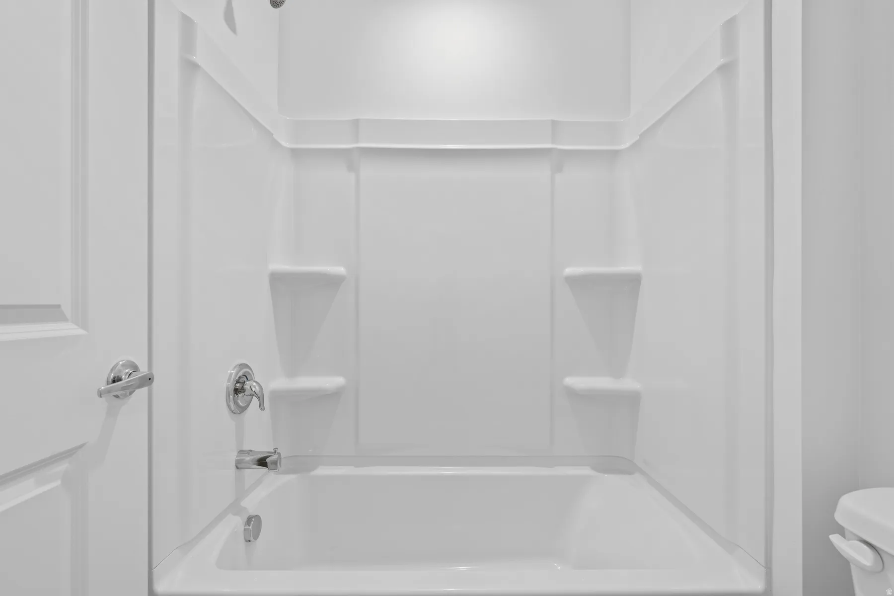 White alcove bathtub and shower combination featuring integrated shelving