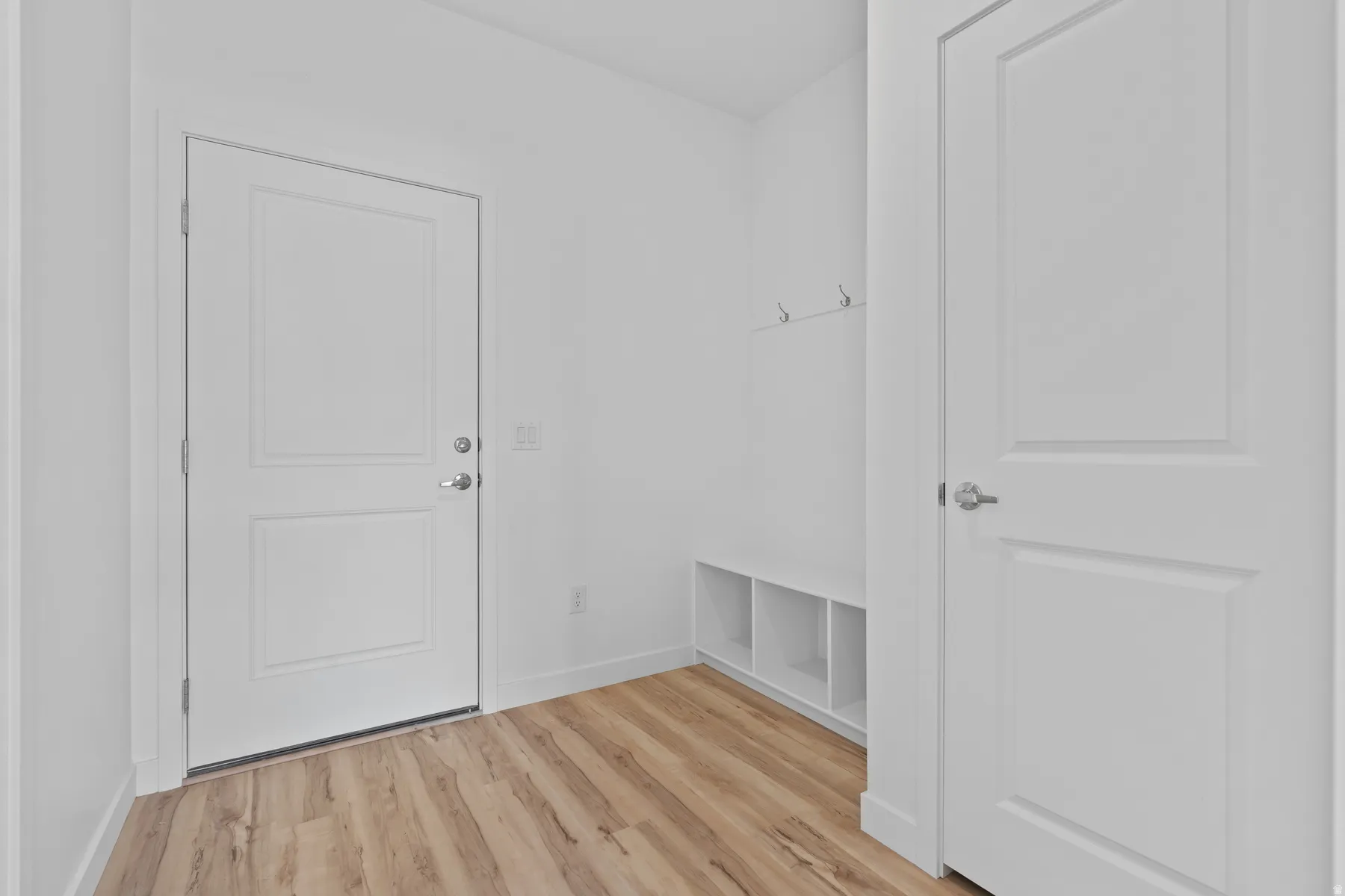 Entryway featuring wood-finish flooring, white paneled doors, and a built-in bench with cubby storage