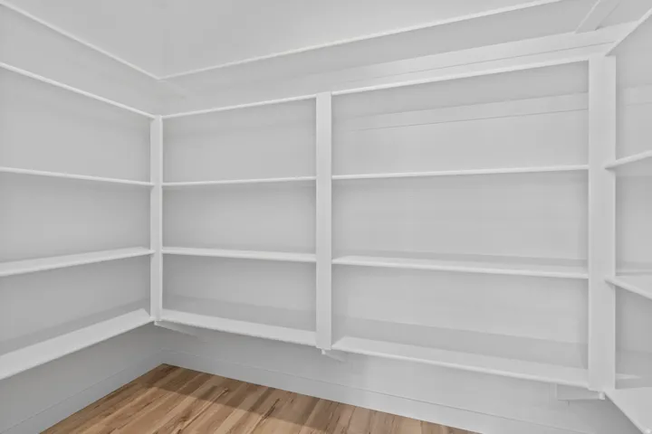 Built-in shelving unit featuring multiple white painted shelves, detailed trim work, white painted walls, and wood-finish flooring