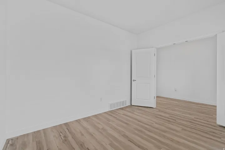 Bright interior featuring wood-finish flooring, white baseboards, and a white interior door with a silver handle