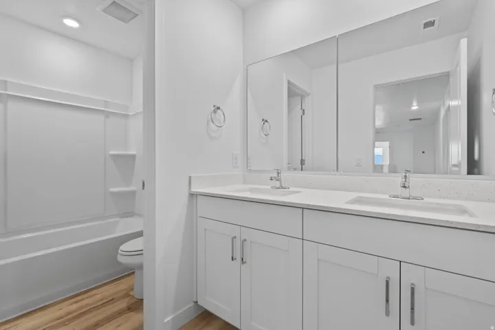 Bathroom featuring a dual vanity with white cabinetry and light-toned countertops, a large wall-mounted mirror, and wood-finish flooring