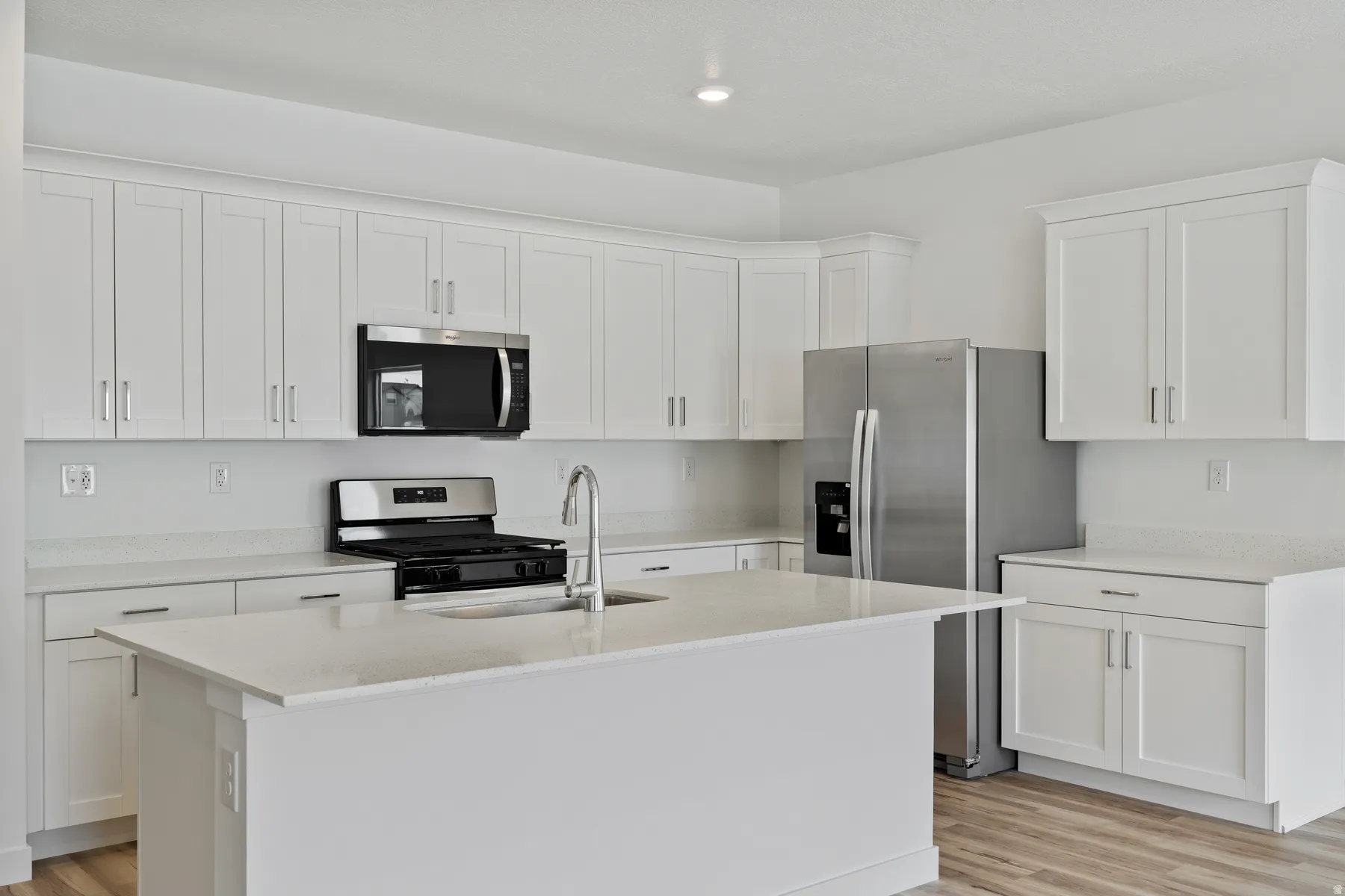 Kitchen featuring an expansive white island, stainless steel appliances, white cabinetry, light-toned countertops, and wood-finish flooring
