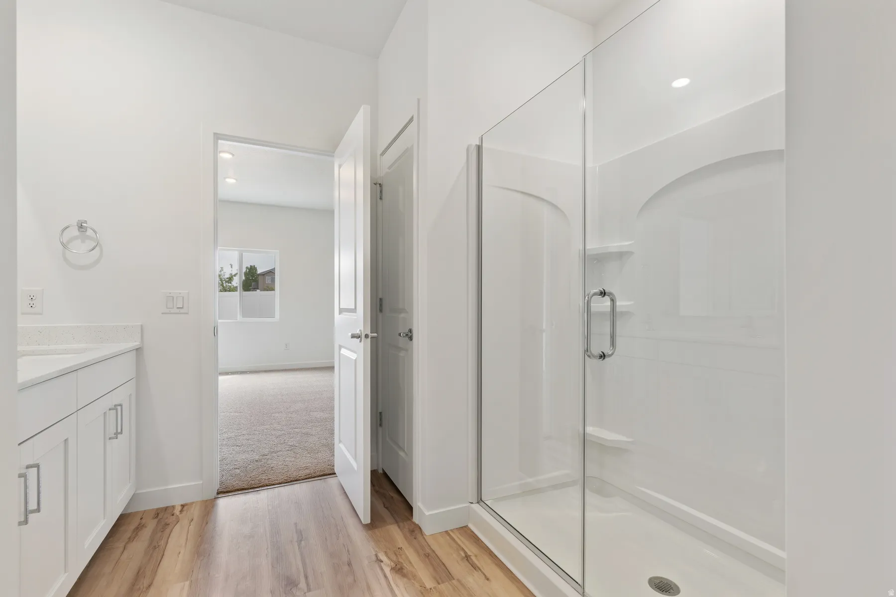 Bright bathroom featuring a glass-enclosed shower with integrated shelving, white vanity with stone-finish countertop, wood-finish flooring, and recessed lighting