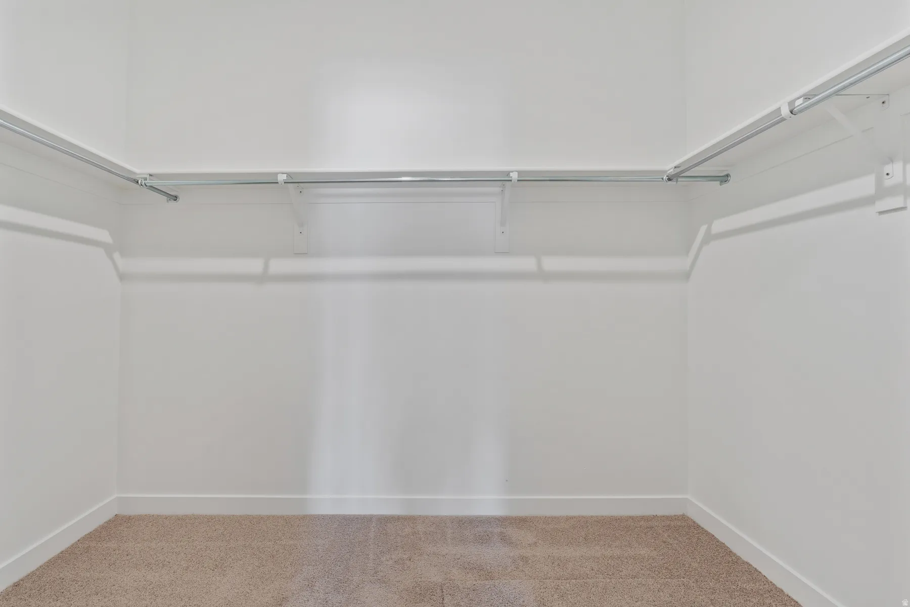 Spacious closet featuring neutral tone carpet, white baseboards, and built-in shelving with hanging rods