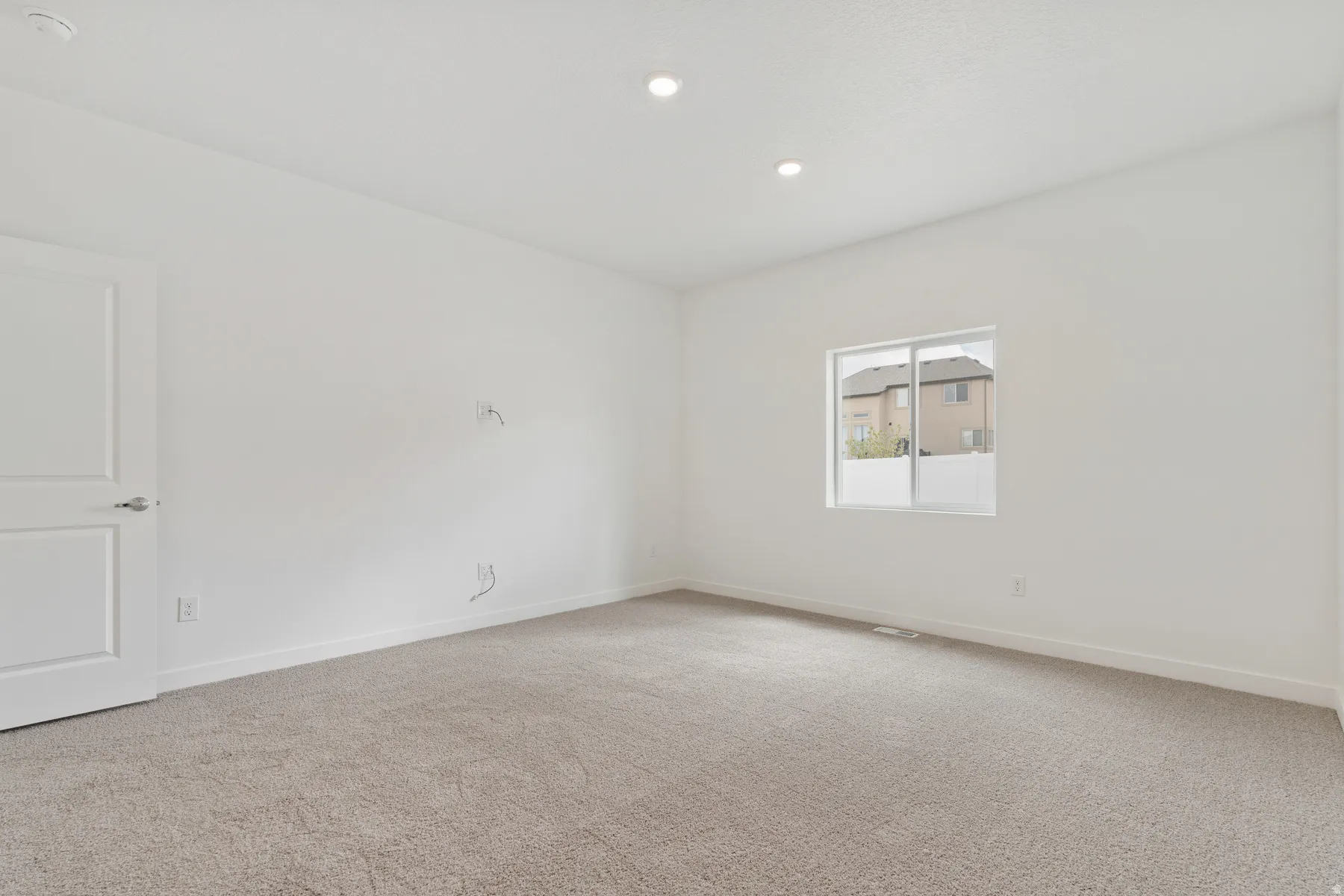 Spacious room featuring neutral carpeting, white walls, recessed ceiling lighting, a single window, and a white paneled door