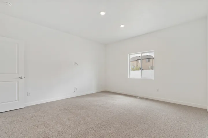 Spacious room featuring neutral carpeting, white walls, recessed ceiling lighting, a single window, and a white paneled door