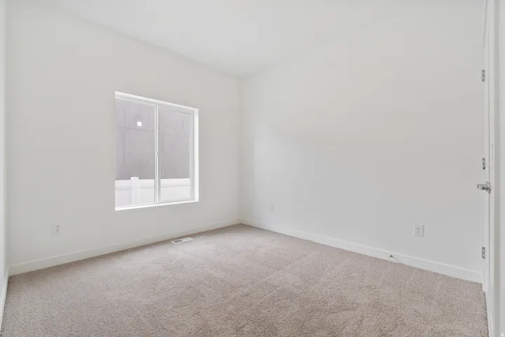 Neutral-toned carpet flooring, white painted walls, white trim, a single window with white framing, and a white door with a silver handle