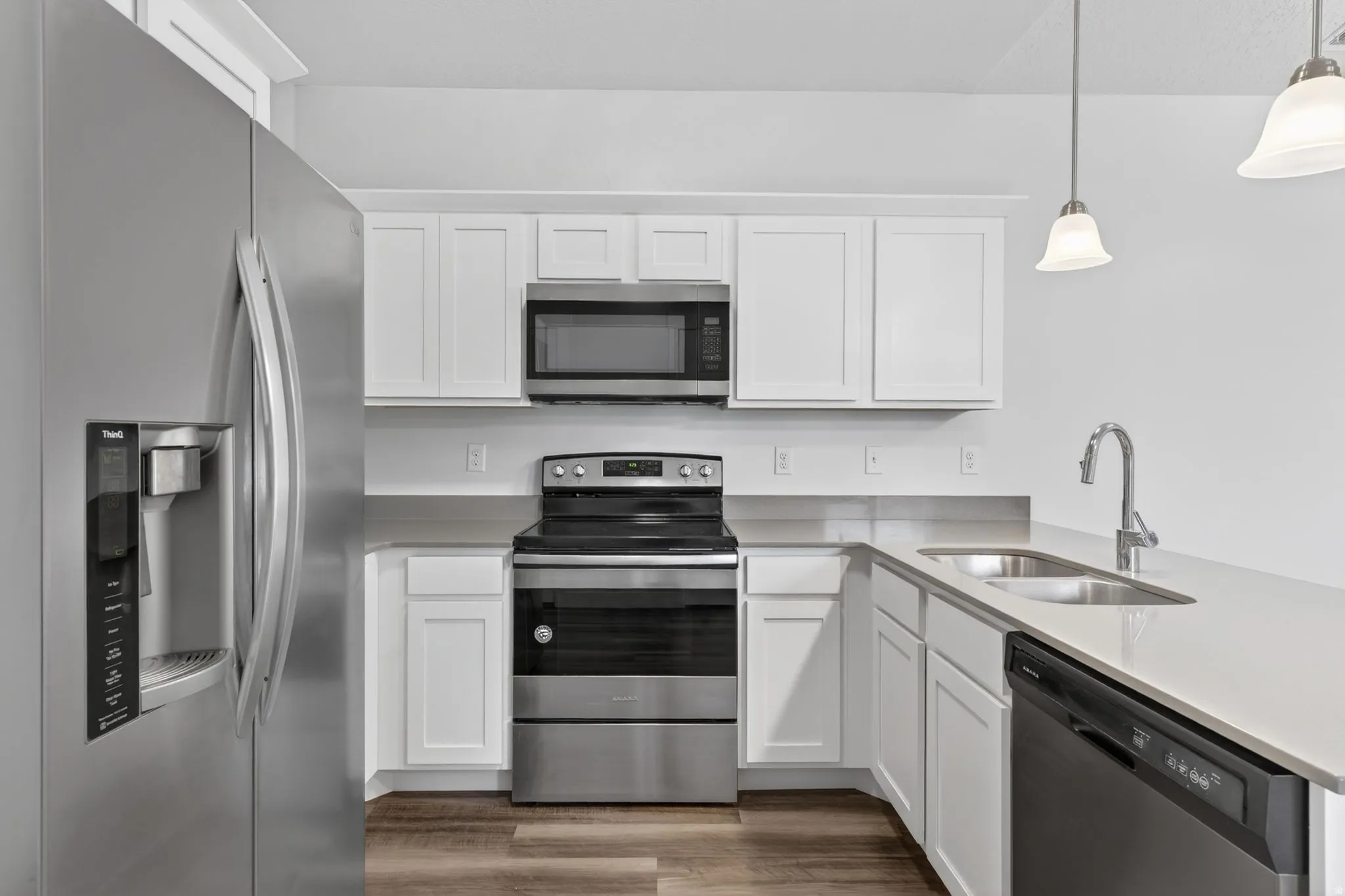 Kitchen featuring stainless steel appliances, white cabinetry, pendant lighting, and light wood-type flooring