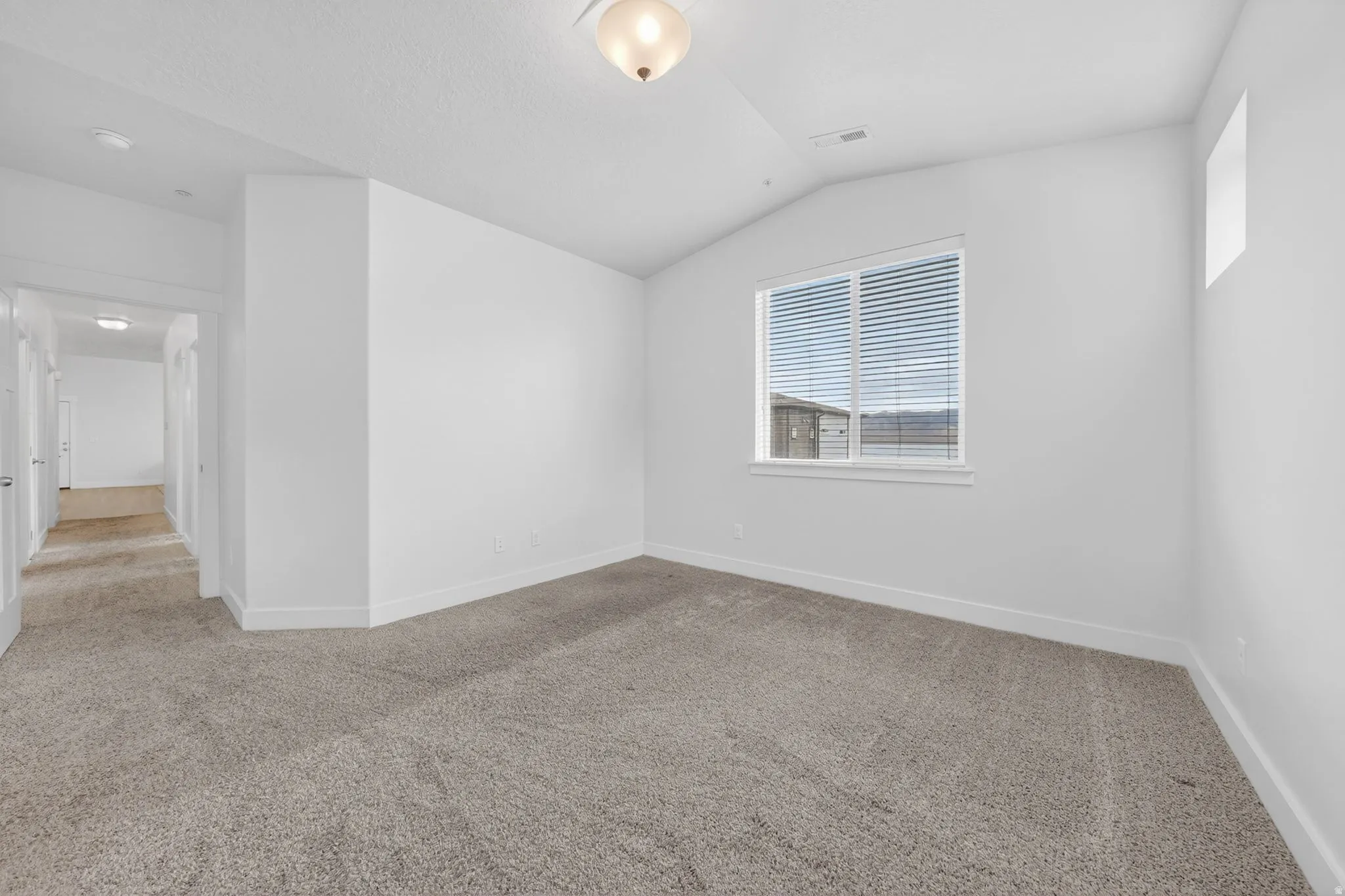 Spare room featuring light colored carpet and vaulted ceiling