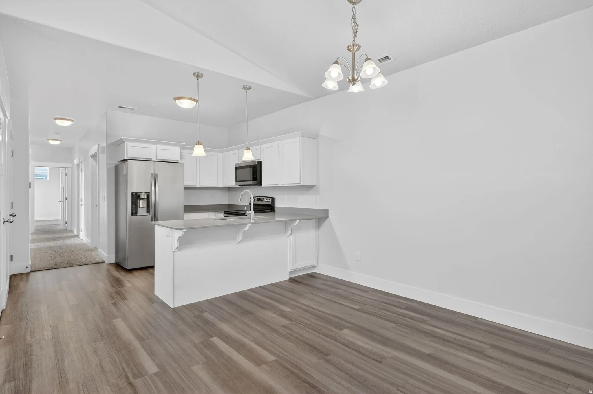 Kitchen with white cabinetry, stainless steel appliances, a peninsula, a breakfast bar, and suspended lighting