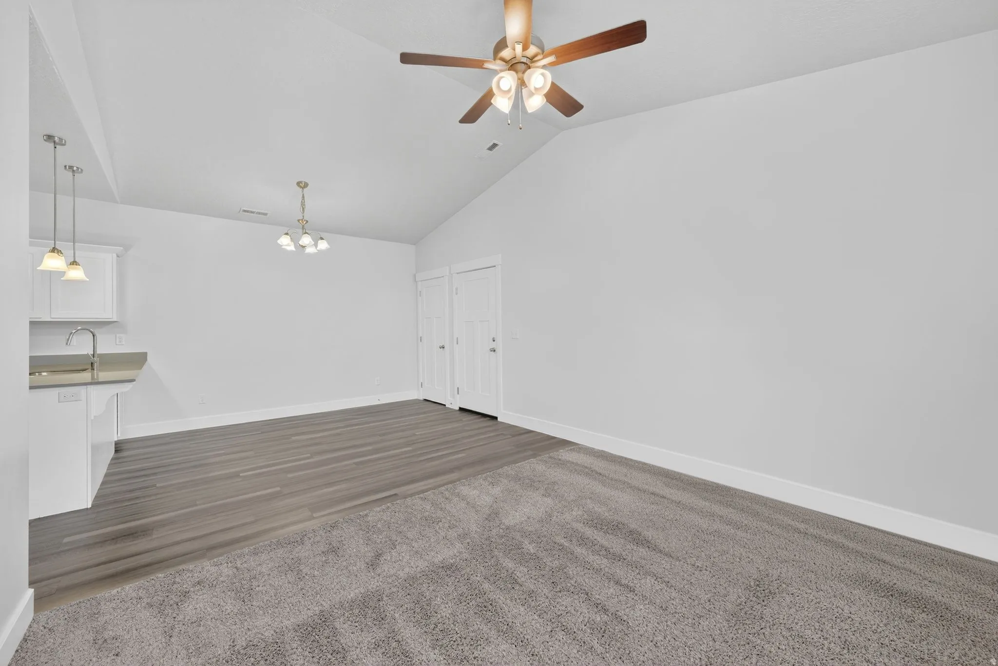 Unfurnished living room with ceiling fan, suspended lighting, vaulted ceiling, and dark carpet
