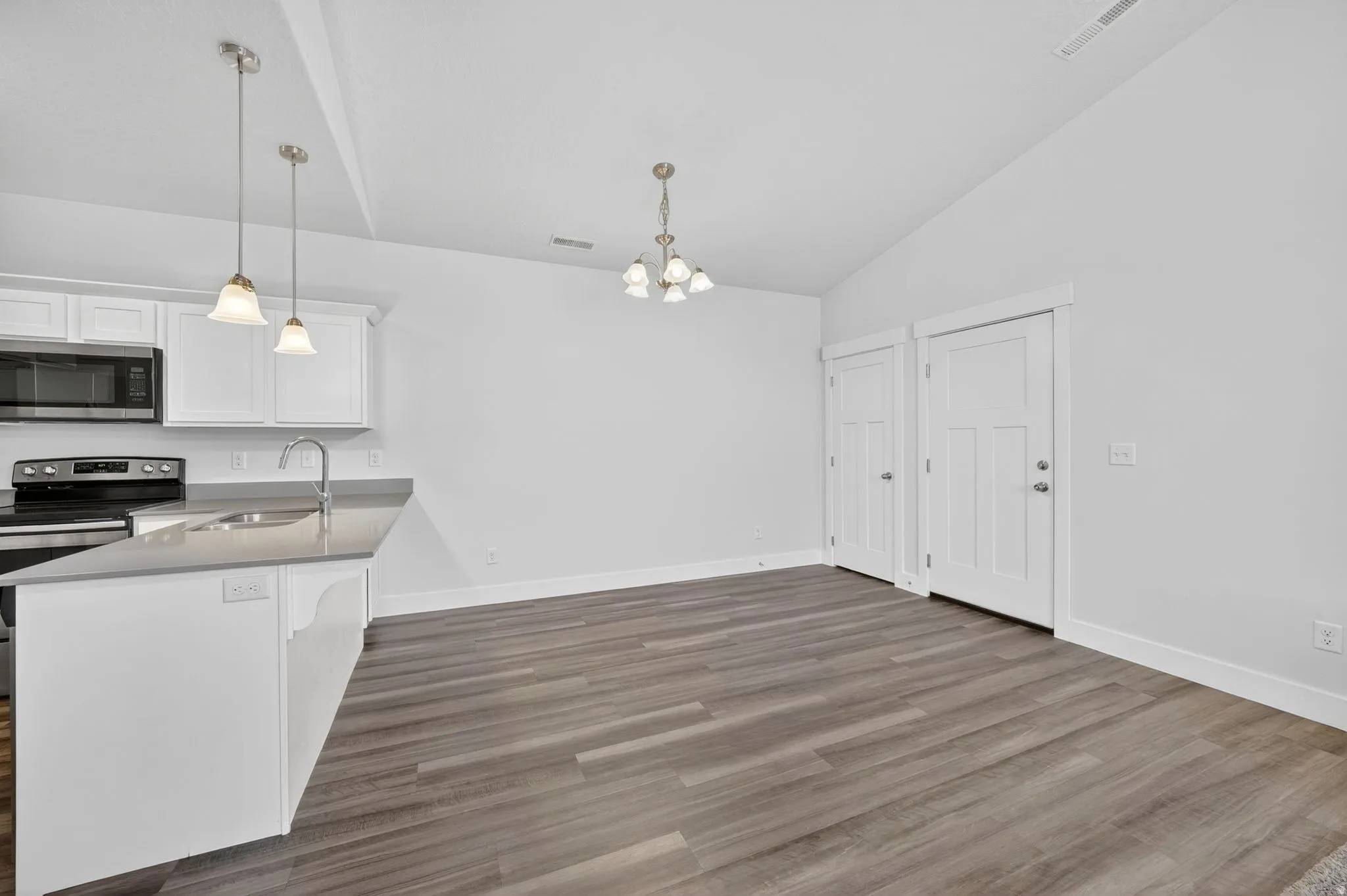 Kitchen featuring white cabinets, stainless steel appliances, vaulted ceiling, suspended lighting, and dark wood-style flooring