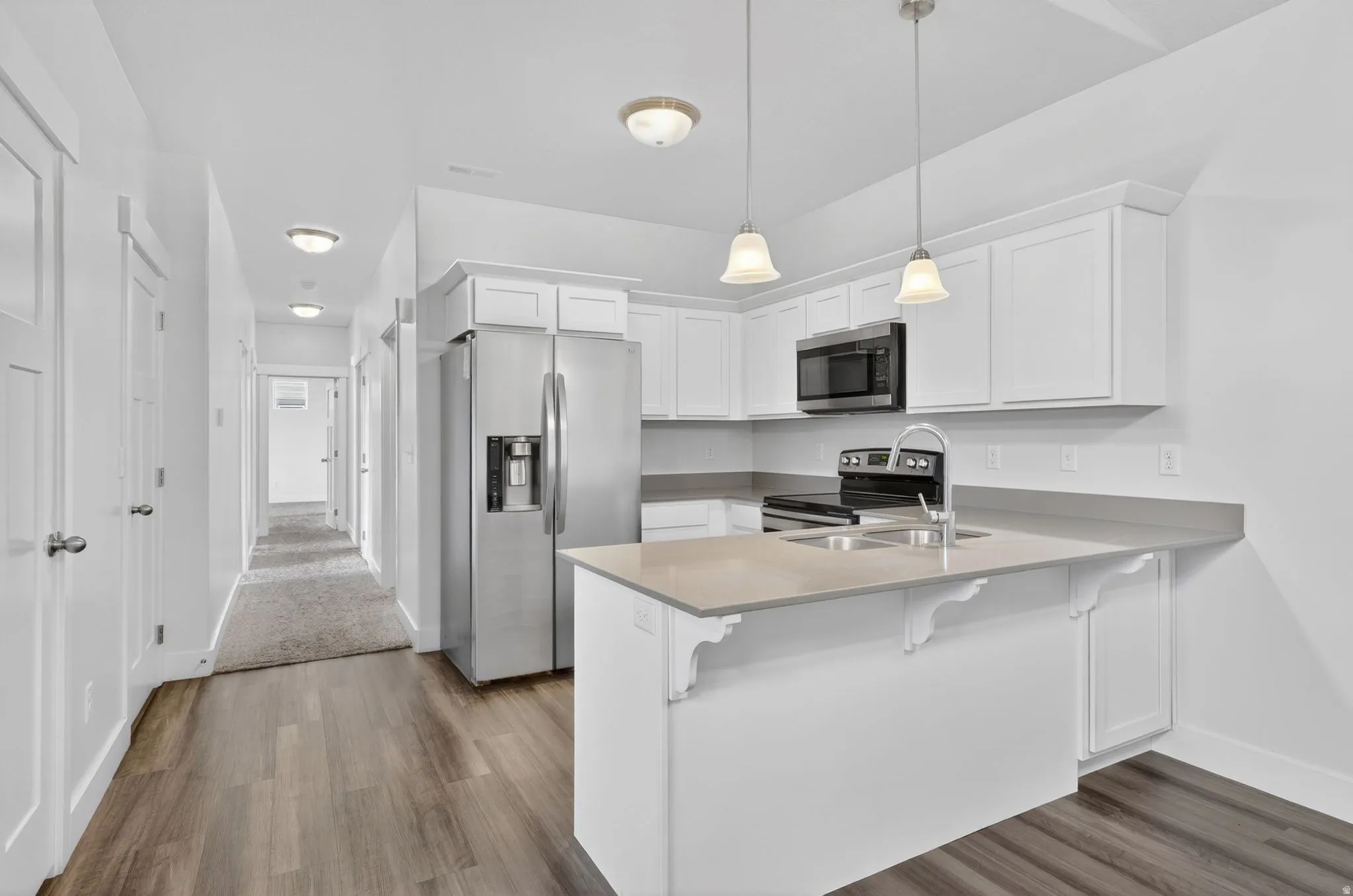 Kitchen with a kitchen breakfast bar, white cabinets, a peninsula, stainless steel appliances, and dark wood-style flooring