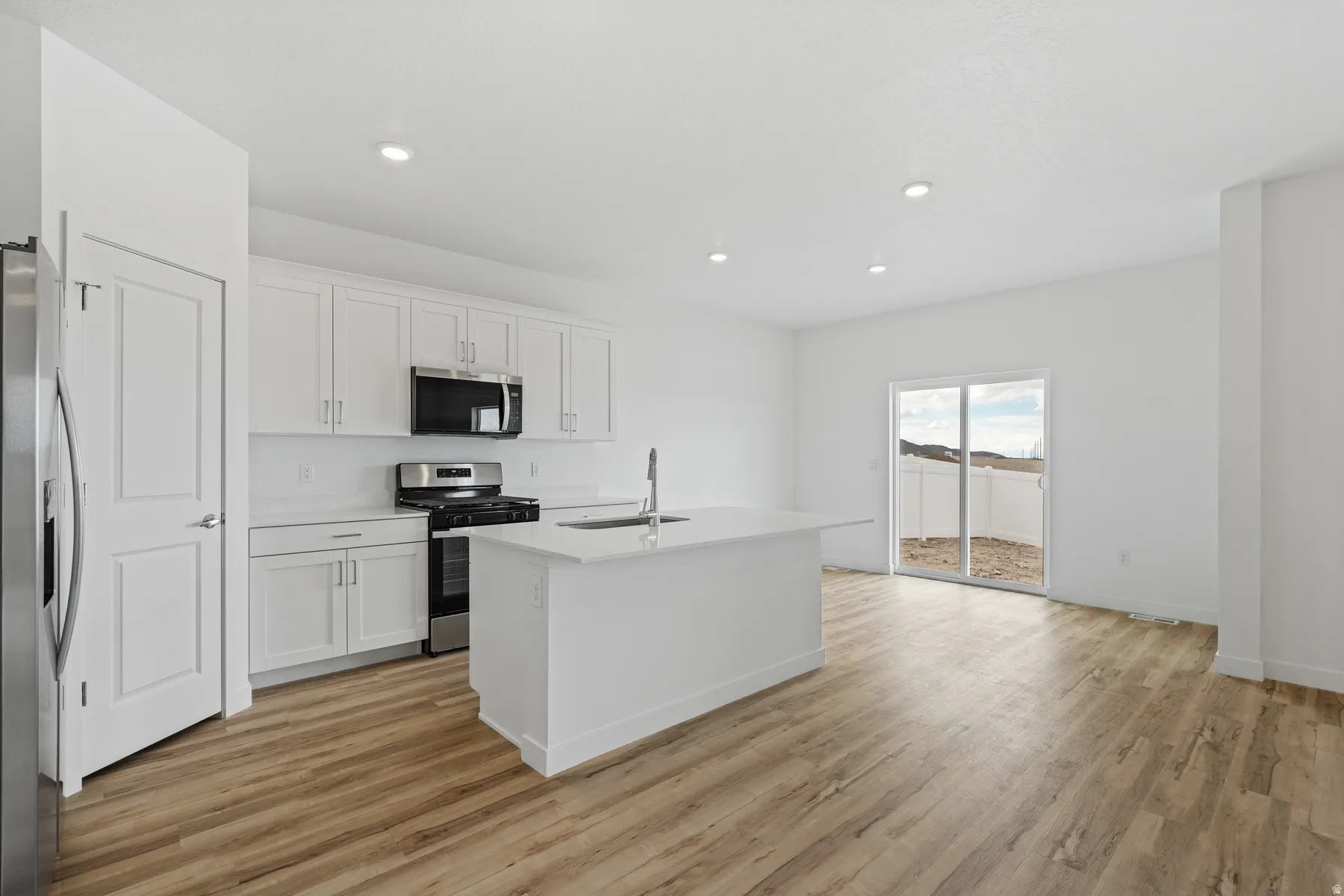 Open-concept kitchen featuring white cabinetry, stainless steel appliances, a central island with an undermount sink, recessed lighting, and wood-finish flooring