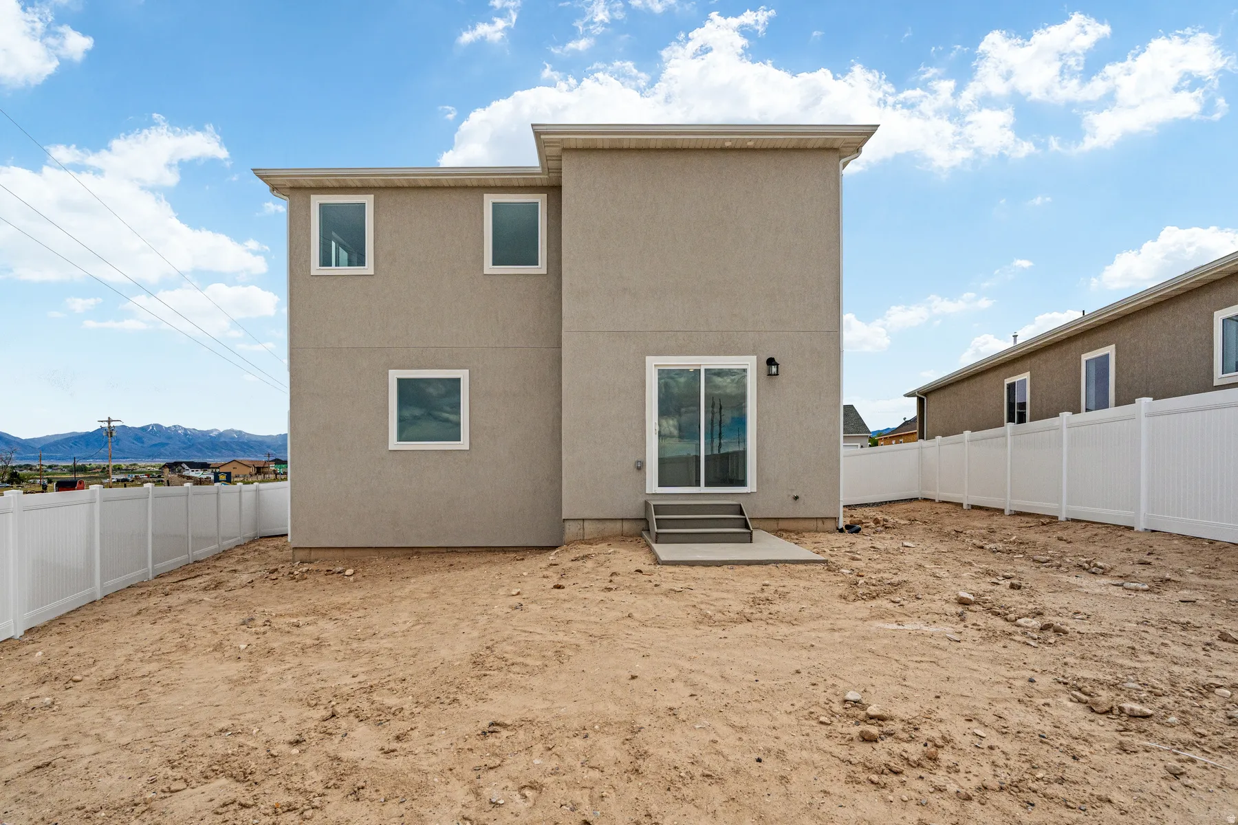 Rear exterior featuring a stucco finish, multiple square windows with white trim, and a sliding glass door leading to a concrete patio
