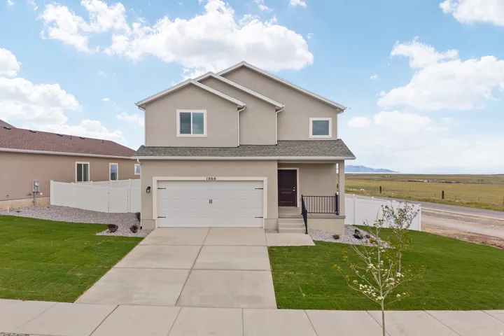 Contemporary two-story residence featuring a neutral stucco exterior, a two-car garage, a covered front porch with dark railings, a concrete driveway, and a manicured lawn