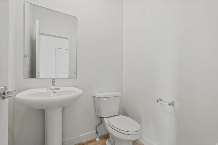 Bathroom featuring a pedestal sink with a chrome faucet, a rectangular wall-mounted mirror, and a white toilet