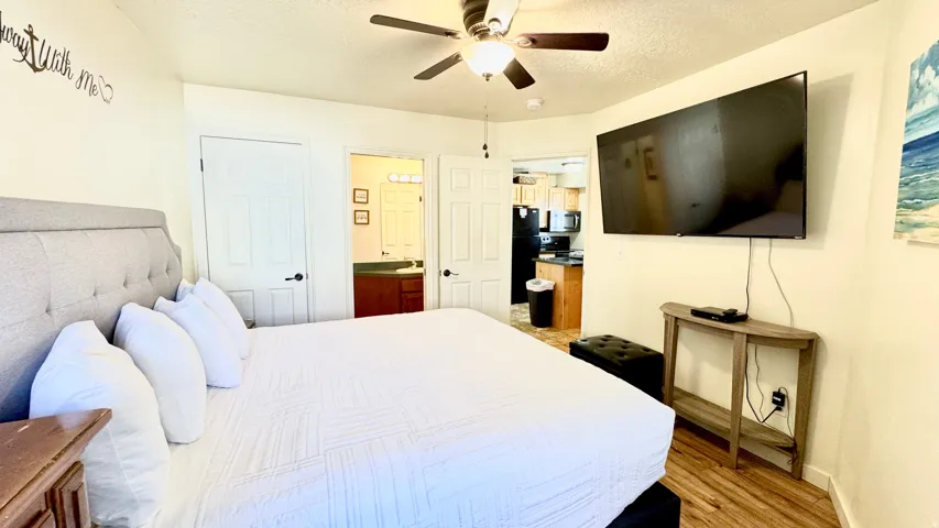 Bedroom with a textured ceiling, light wood-style floors, connected bathroom, freestanding refrigerator, and ceiling fan