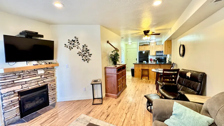 Living room featuring light wood-type flooring, a textured ceiling, a ceiling fan, a stone fireplace, and recessed lighting