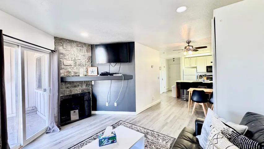 Living room with light wood-type flooring, a stone fireplace, a ceiling fan, and a textured ceiling