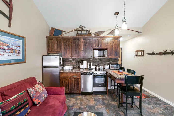 Kitchen with freestanding refrigerator, dark wood finish cabinets, lofted ceiling, stone finish flooring, and electric range