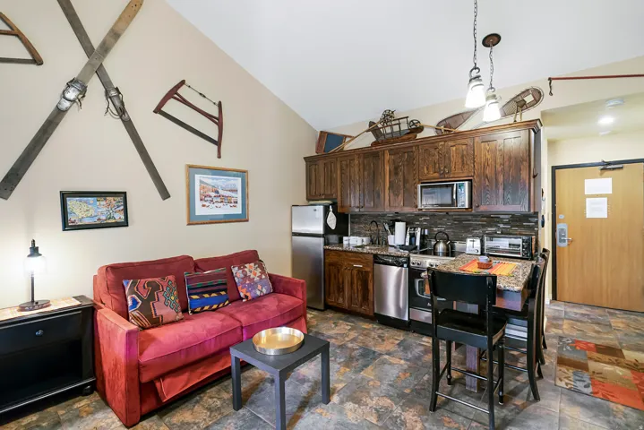 Kitchen featuring dark wood finish cabinets, vaulted ceiling, stainless steel appliances, dark stone finish flooring, and backsplash