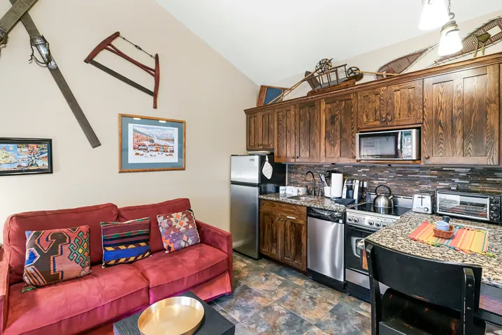 Kitchen featuring stainless steel appliances, dark wood finish cabinetry, stone finish floors, light stone countertops, and open floor plan