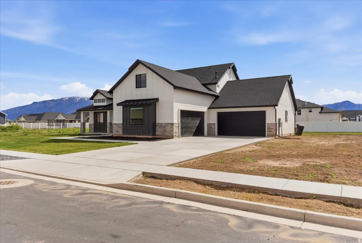 Modern inspired farmhouse with a mountain view, driveway, an attached garage, stone siding, and a residential view