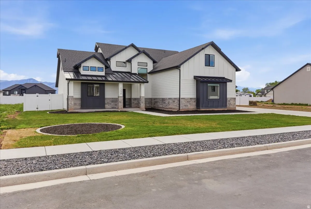 Modern farmhouse style home featuring a standing seam roof, a porch, a gate, stone siding, and board and batten siding