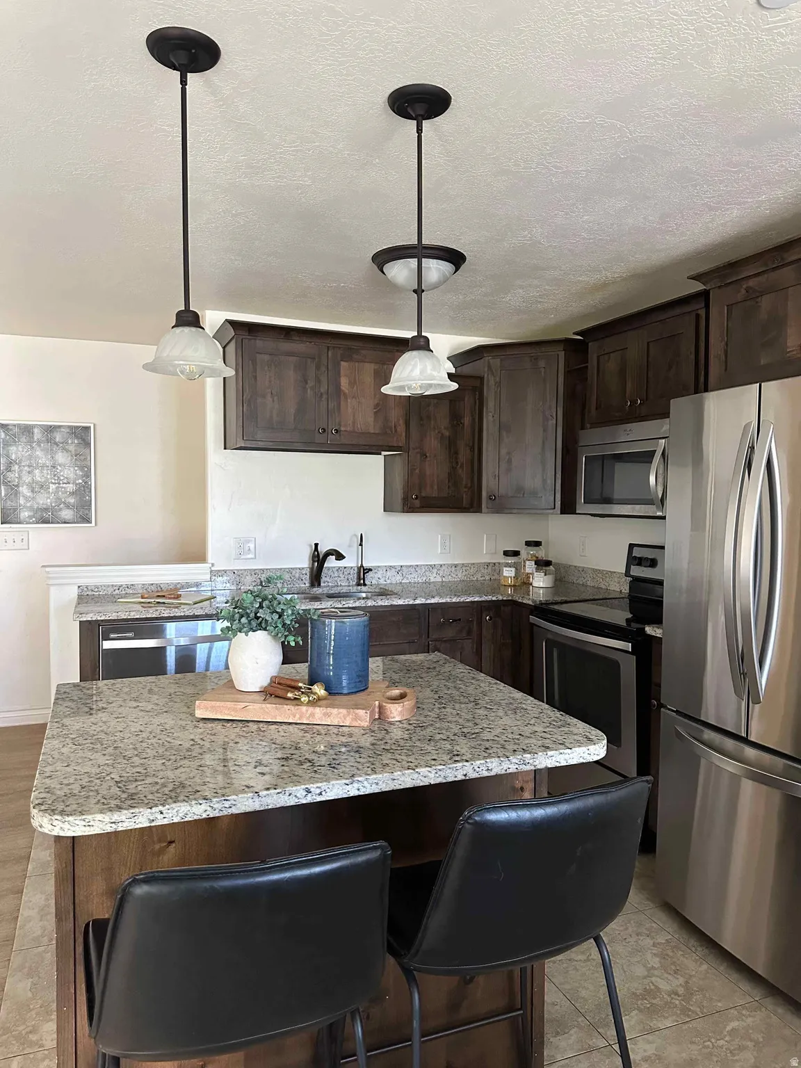 Kitchen featuring dark wood finish cabinets, a center island, stainless steel appliances, a kitchen bar, and a textured ceiling