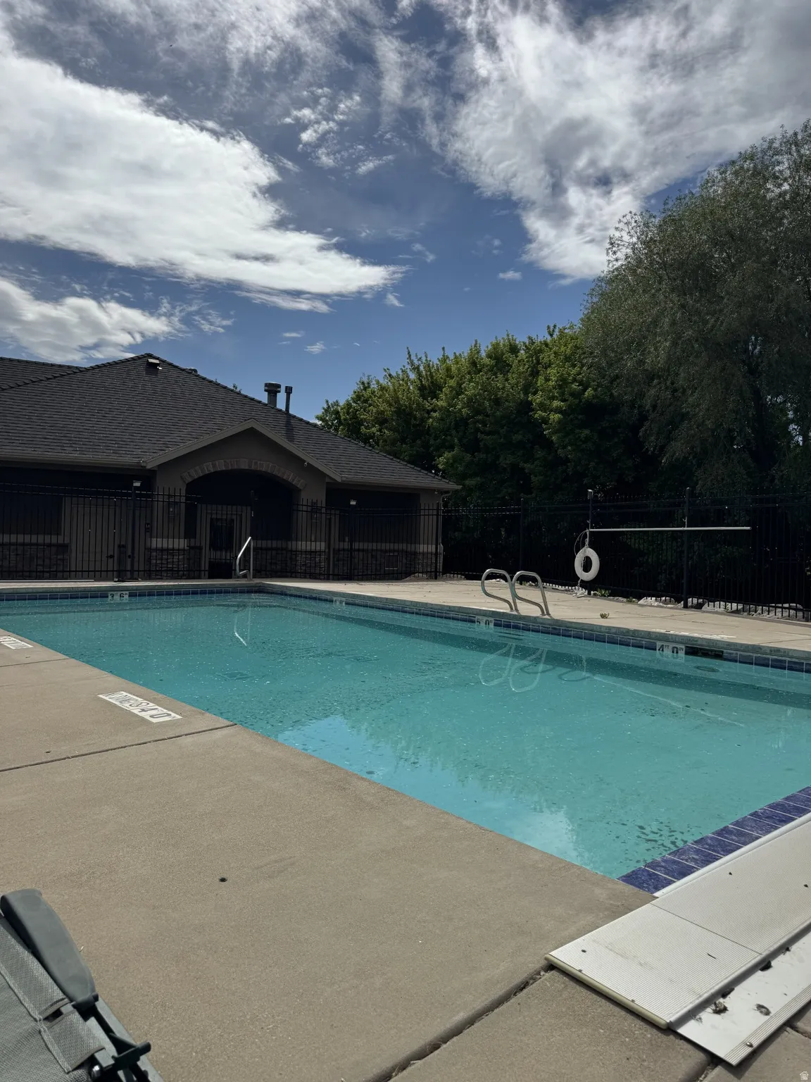 Outdoor swimming pool with concrete decking, surrounded by a black metal fence