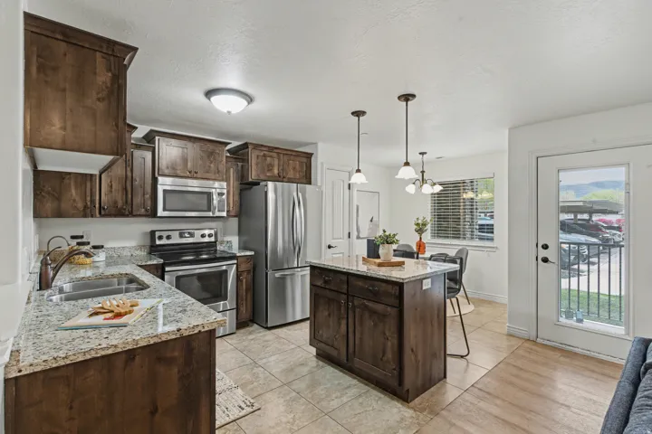 Kitchen with dark wood finish cabinets, stainless steel appliances, light stone countertops, a kitchen island, and light tile patterned floors