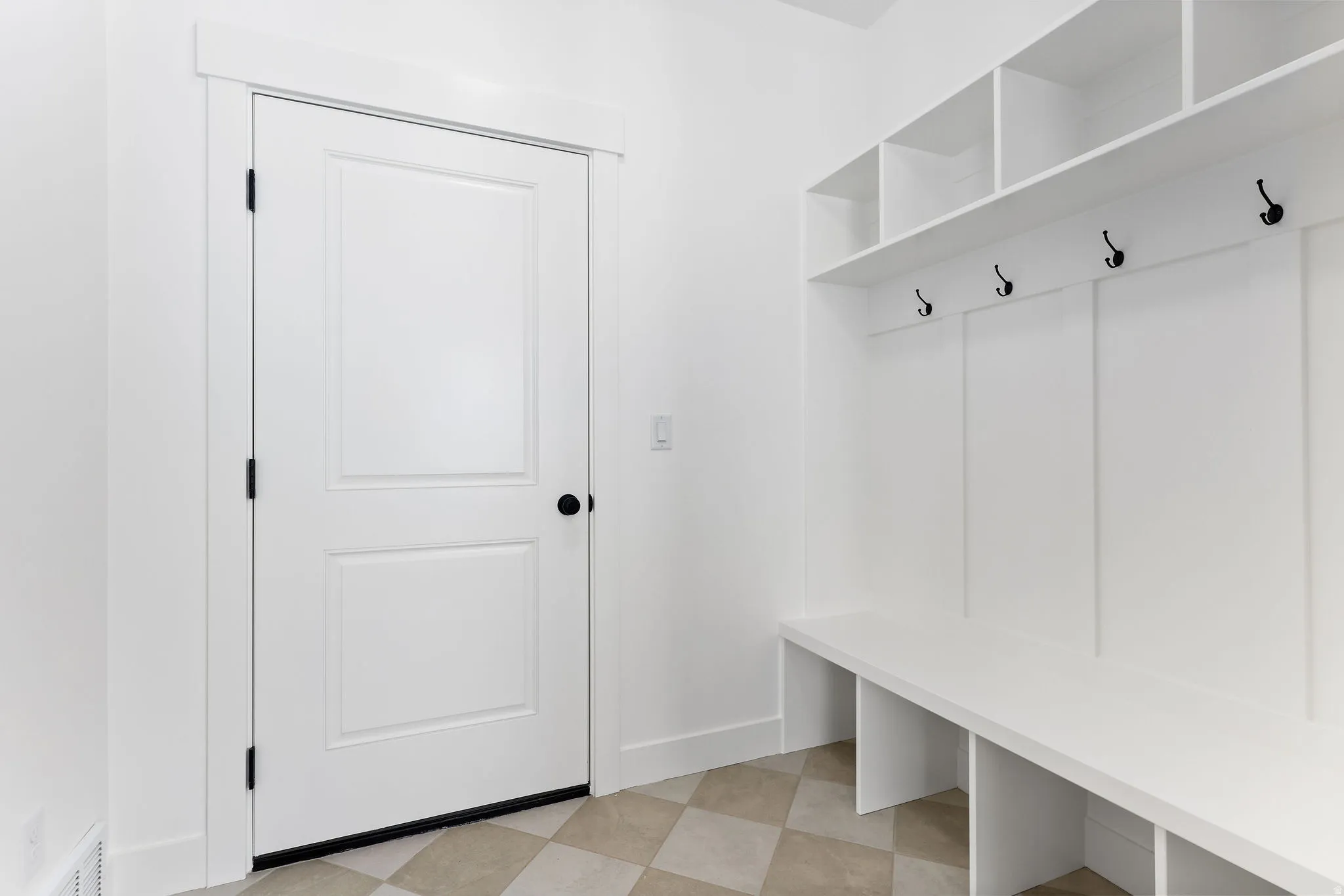 Entryway featuring built-in white storage cubbies, a bench, and a coat rack with black hooks